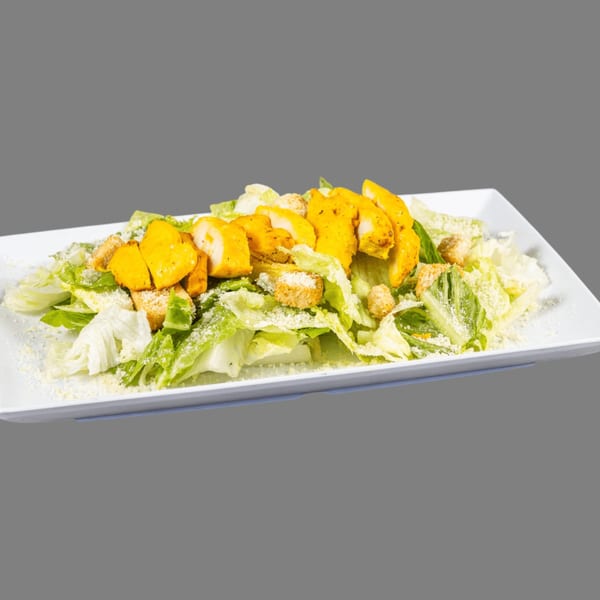Caesar salad with grilled chicken, croutons, and parmesan cheese on a white rectangular plate.