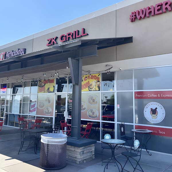 Exterior of ZK Grill, a Mediterranean restaurant, with outdoor seating and large window advertisements.