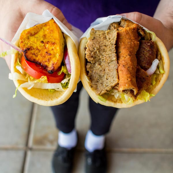 Hands holding two ZK Grill Mediterranean gyros, one with chicken and the other with meat.